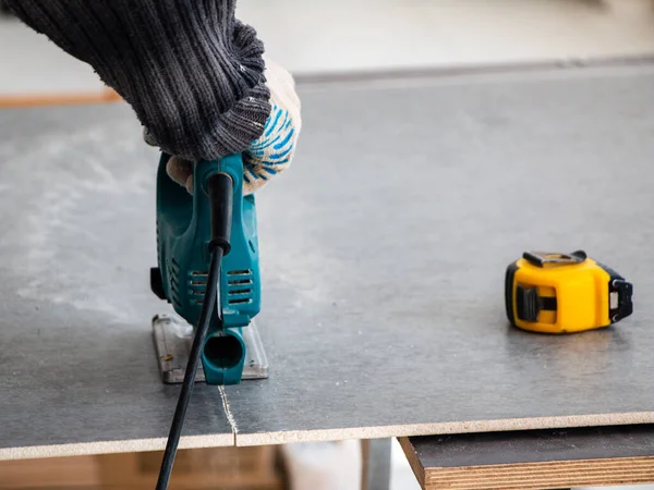 male hands of a construction worker sawing and cutting parts with an electric hand jigsaw from a panel. the process of cutting a building board for interior decoration with an electric jigsaw