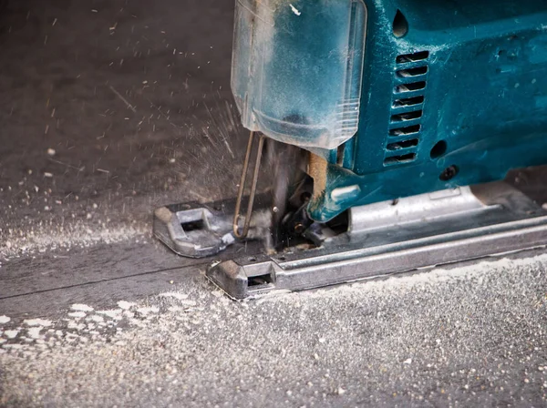 Bir inşaat işçisinin elleri elektrikli bir yapbozun parçalarını kesip biçiyor. İç dekorasyon için bir yapı tahtasını elektrikli bir yap-boz ile kesme işlemi