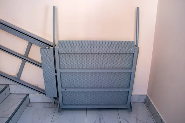 iron gray electric wheelchair lift with a ramp and a chain mechanism for lifting along the stairs, for lifting wheelchairs to the floor above.