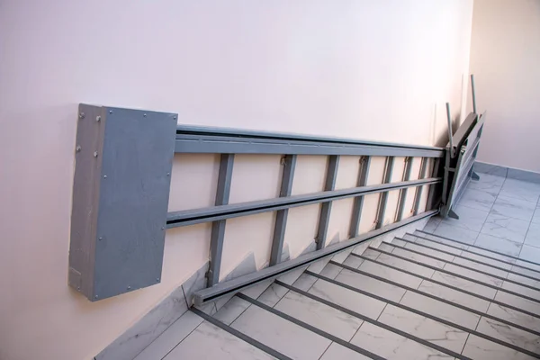 iron gray electric wheelchair lift with a ramp and a chain mechanism for lifting along the stairs, for lifting wheelchairs to the floor above.