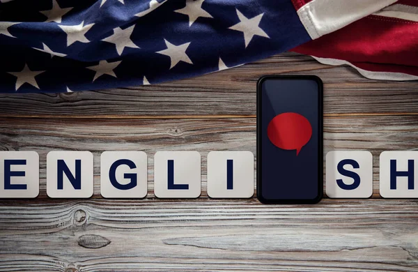 American English language Concept. Mobile Phone with Speech Bubble and USA Flag lay on Vintage Wooden background. Online Learning. Speak English. Top View
