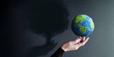 World Earth Day, ESG Concept. Green Energy, Renewable and Sustainable Resources. Environmental and Ecology Care. Hand Gesture Levitating a Green Handmade Globe. Big Tree Shadow shading on the Wall clipart