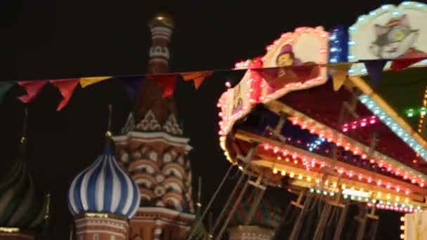 モスクワの赤の広場にある大きなカルーセル 街のクリスマスマーケット人々は休日に一緒に楽しみを持っています バジル大聖堂を背景に — ストック動画