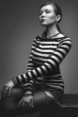 Gri stüdyoda siyah bir kübün üzerinde poz veren güzel seksi, zayıf kız.