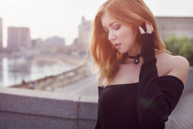 Dar siyah elbiseli genç bir kız şehirde yürüyor. Köprüde.