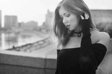 Dar siyah elbiseli genç bir kız şehirde yürüyor. Köprüde.