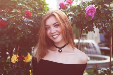 Siyah elbiseli, kızıl saçlı kız. Gül çalıları..