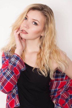 Beyaz duvarda poz veren güzel bir kız. Beyaz duvara karşı duran şort ve gömlekli.