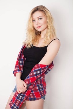 Beyaz duvarda poz veren güzel bir kız. Beyaz duvara karşı duran şort ve gömlekli.. 