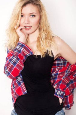 Beyaz duvarda poz veren güzel bir kız. Beyaz duvara karşı duran şort ve gömlekli.