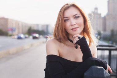 Dar siyah elbiseli genç bir kız şehirde yürüyor. Köprüde.