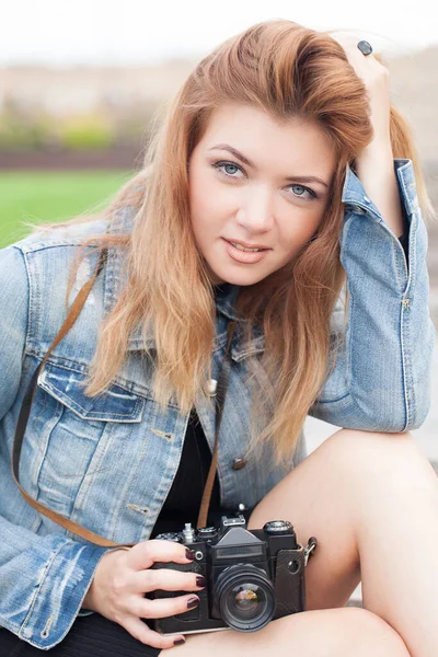 年轻的女摄影师穿着一件旧照相机的牛仔裤夹克在街上走着 — 图库照片