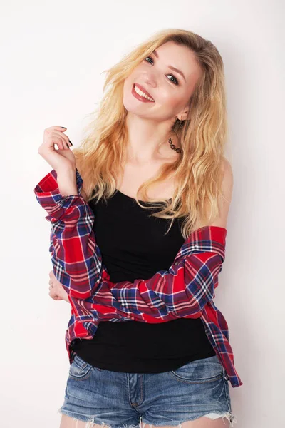 Beyaz duvarda poz veren güzel bir kız. Beyaz duvara karşı duran şort ve gömlekli.