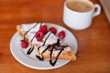 Pudra şekerli elmalı turta, taze ahududu ve çikolatalı krema. Bir fincan sade kahve.