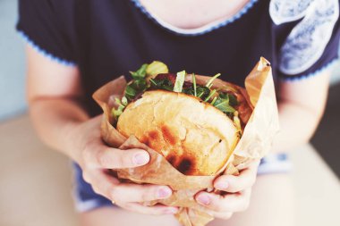 Kız büyük bir hamburger tutuyor. Yumuşak bulanık arkaplan. Yaşam tarzı