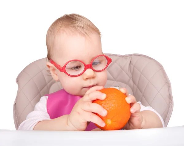 Little child sitting in a chair and plays with orange fruit — Stock Photo, Image