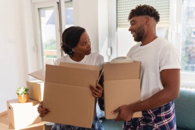 Oturma odasında karton kutular tutarken gülümseyen bir çift.