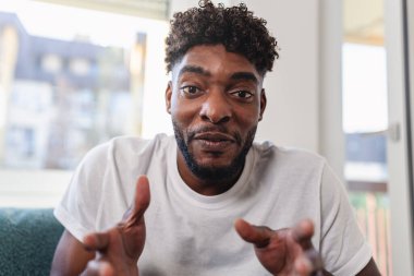 Gülümseyen adam koltukta otururken el kol hareketi yapıyor.