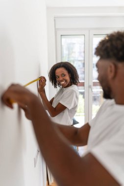 Gülümserken ve birlikte çalışırken duvarı ölçen iki kişi.