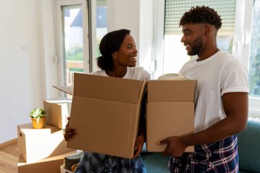 Oturma odasında karton kutular tutarken gülümseyen bir çift.