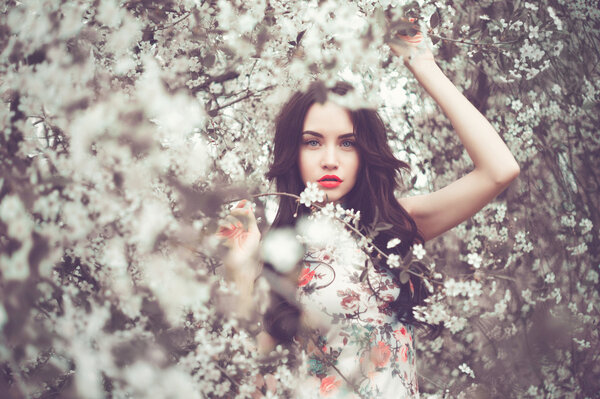 Outdoors fashion photo of beautiful young lady in the garden of cherry blossoms