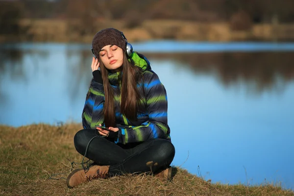 Молодая девушка сидит на земле и слушает музыку после похода — стоковое фото