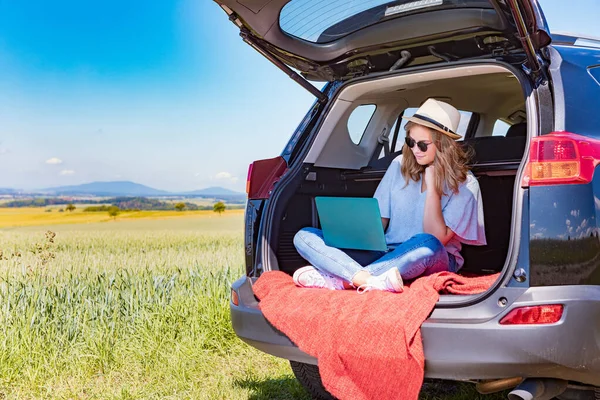 a young girl with the laptop in  a car on the countryside journey