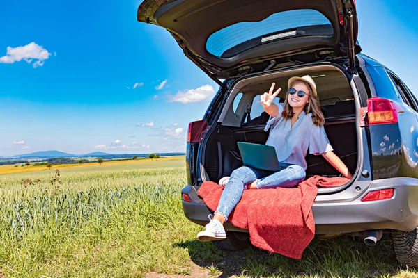 a young girl with the laptop in  a car on the countryside journey