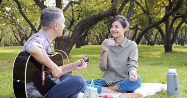 Gitarlı mutlu çift çimenlikteki parkta piknik yapıyor. Aşk, tatil ve yaz konsepti