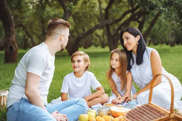 緑の庭でピクニック中に芝生でリラックスしている2人の子供を持つ幸せな家族 ロイヤリティフリーのストック写真
