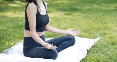 Nilüfer pozisyonunda meditasyon yapan, parktaki çimlerin üzerinde oturan tanınmamış genç bir kadının yakın çekimi. Yoga ve uyum kavramı.