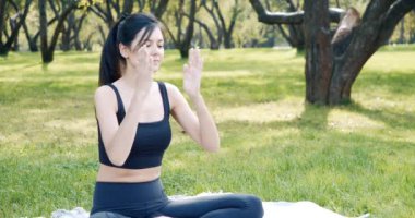 Nilüfer pozisyonunda meditasyon yapan genç bir kadın parkta çimlerin üzerinde otururken derin derin nefes alıyor. Yoga ve uyum kavramı.