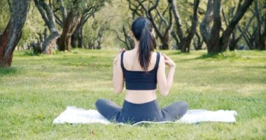Parktaki çimenlerde otururken esneme hareketleri yapan genç bir kadın. Arkadan bak. Yoga ve sağlıklı yaşam tarzı konsepti.