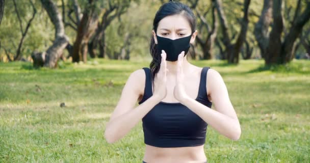晴れた日に公園で黒い保護マスクを身に着けている間 若い女性は蓮の位置でヨガ瞑想を練習します 流行で健康的なライフスタイルのコンセプト — ストック動画