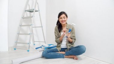 Genç, gülümseyen bir kadının portresi boya silindirleri hakkında konuşuyor ve video bloğu için bir video kaydediyor. Bloglama, sosyal medya ve yenileme kavramı