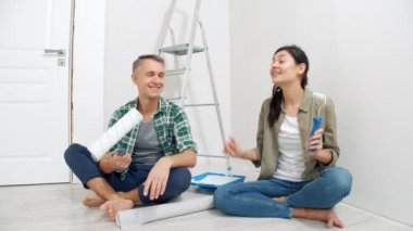 Genç mutlu çift ellerinde boya silindirleri ve video kayıtları tutuyorlar. Yenileme, blog yazma ve sosyal medya kavramı