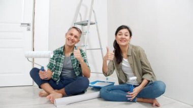 Genç mutlu çift ellerinde boya silindirleri ve video kayıtları tutuyorlar. Yenileme, blog yazma ve sosyal medya kavramı