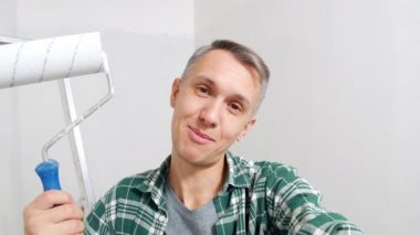 Genç mutlu adam boya silindiri tutuyor ve video kaydediyor ya da yenileme sırasında arkadaşlarıyla internette sohbet ediyor. Bloglama, sosyal medya ve DIY onarım kavramı