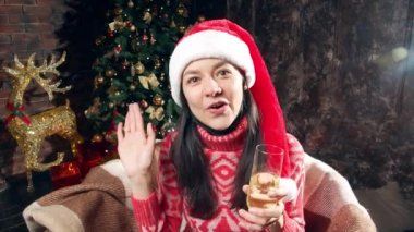 Çenesine koruyucu bir maske takmış, elinde bir kadeh şampanya tutan, kameraya öpücük yollayan ve evinde bir video kaseti kaydeden mutlu bir kadının portresi.