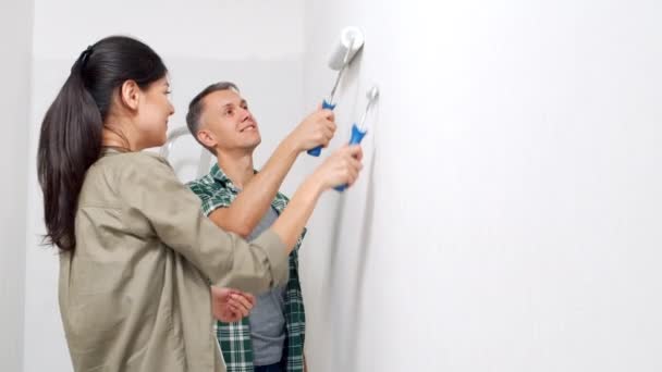 新しい家の塗料ローラーと若い幸せなカップルの絵画の壁 Diy修理コンセプト — ストック動画