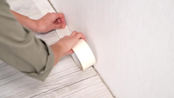家の改装中に壁を塗装する前に保護のために床にマスキングテープを貼り付ける女性の手の閉じる — ストック動画