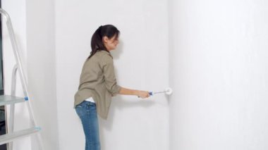 Duvarı silindirle boyayan genç bir kadın. Yeni konut ve DIY yenileme kavramı.