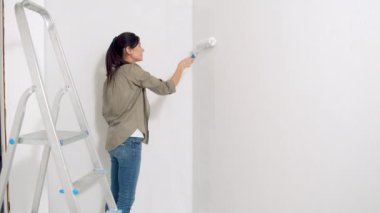Duvarı silindirle boyayan genç bir kadın. Yeni konut ve DIY yenileme kavramı.