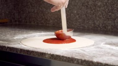 Pizza margarita yapma süreci. Erkek aşçı elleri pizza hamuruna domates sosu sürüyor..