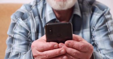 Bir mesaj yazarken ya da sosyal ağlarda sohbet ederken akıllı telefon tutan yaşlı bir erkeğin yakın çekimi.