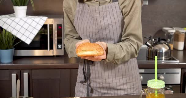 Onherkenbare jonge vrouw in schort snijden broodje in de helft voor het maken van hamburgers in de keuken — Stockvideo