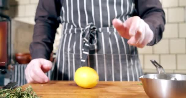Close-up van een onherkenbare mannelijke chef-kok in een schort dat een citroen spint en grijpt op een houten plank. Eten koken in een restaurant — Stockvideo