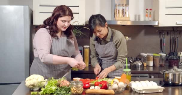 Två attraktiva unga kvinnor förbereder middag med färska grönsaker har roligt chatta och ler i köket hemma. — Stockvideo