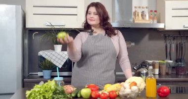 Mutfakta sağlıklı bir akşam yemeği hazırlarken yeşil elma atan iri yarı bir kadının portresi. Diyet ve sağlıklı yemek..