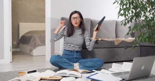 Glade unge kvinne-student som gleder seg over sin suksesslæring fra mange bøker og laptop som sitter på gulvet hjemme. Utdanningsbegrep – stockvideo